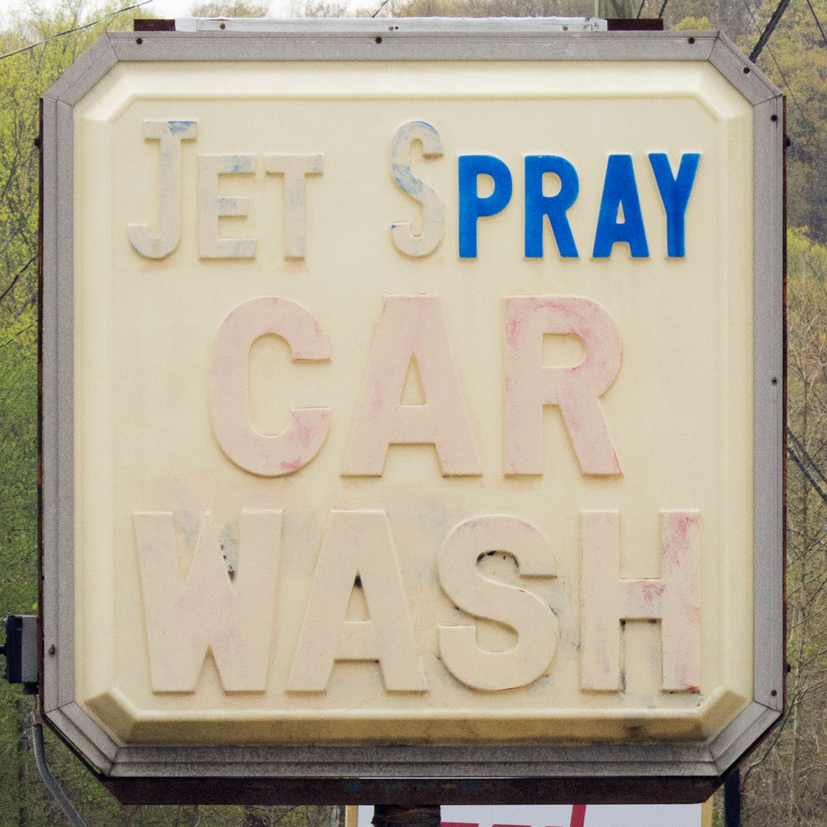 Car wash sign where the words ‘jet spray car wash’ have all faded and someone has painted in certain letters so that the sign now reads ‘pray’