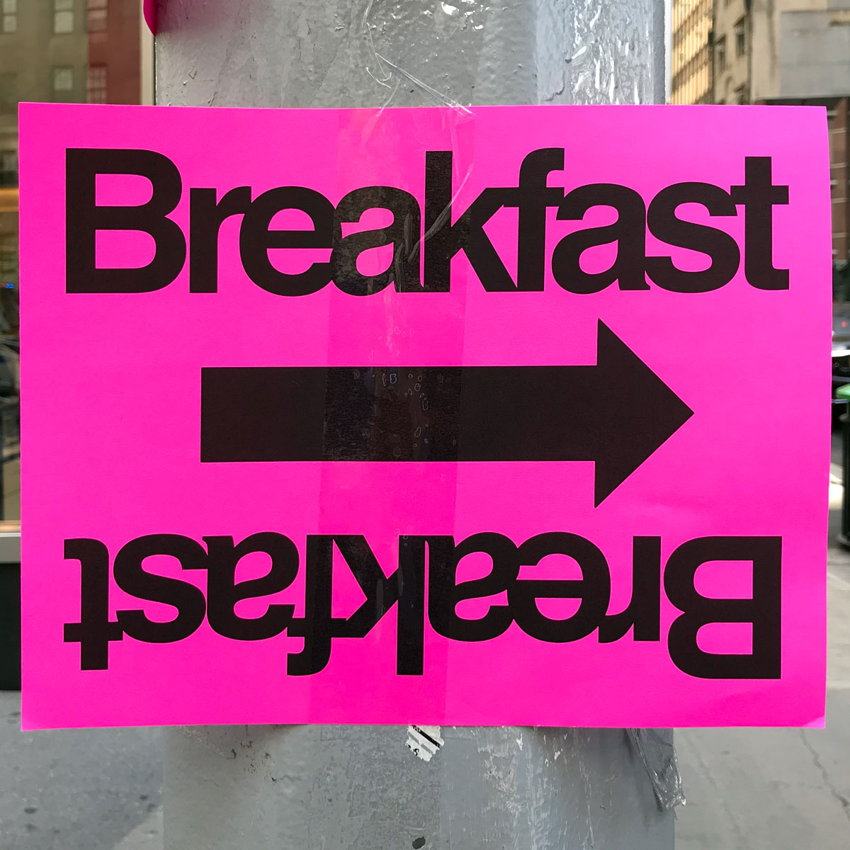 Breakfast sign with an arrow facing right where ‘breakfast’ is written across the top and bottom but flipped over on the bottom so that if the sign were turned 180 degrees it would still be readable