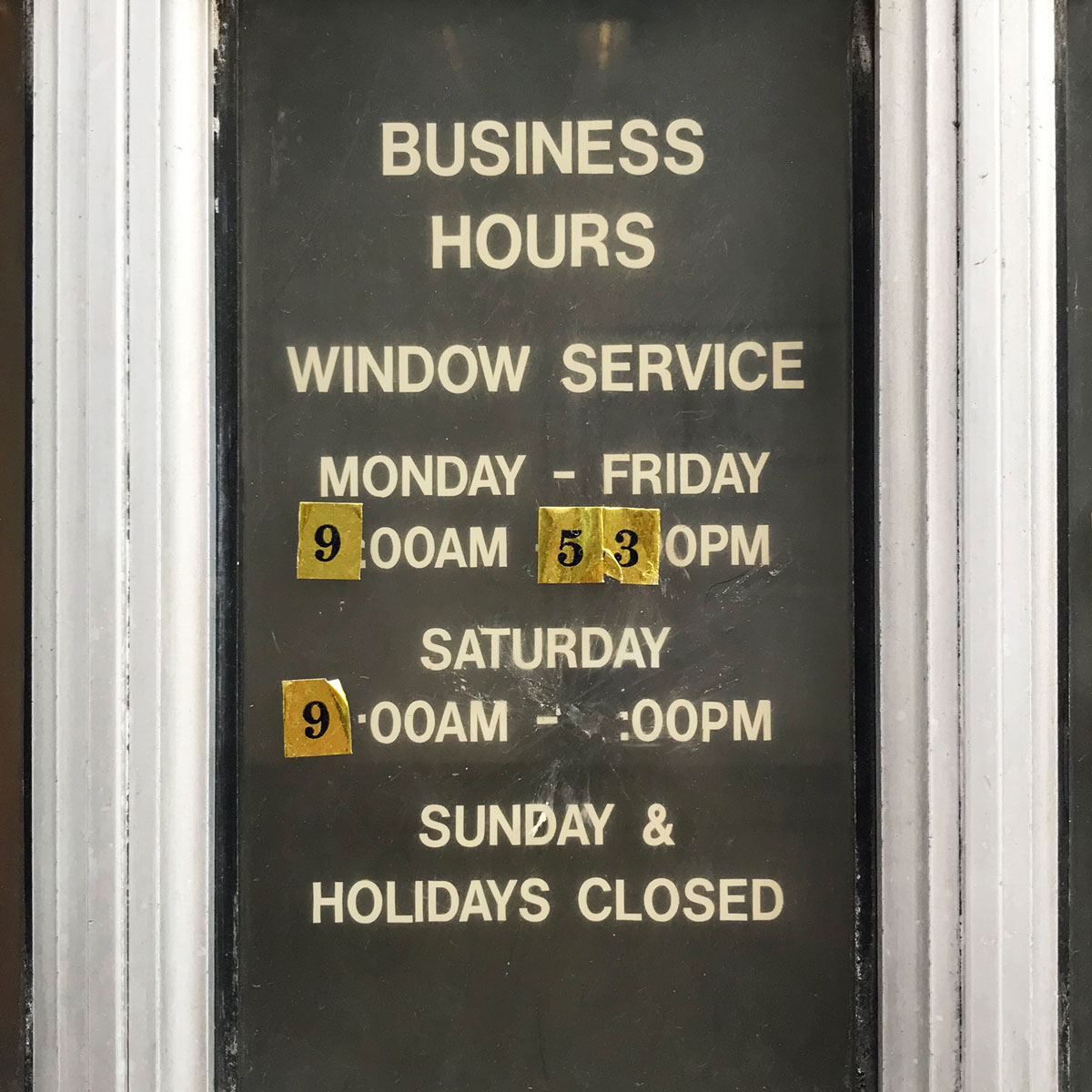 Business hours sign where numbers have been scratched off and replaced with stickers with numbers on them