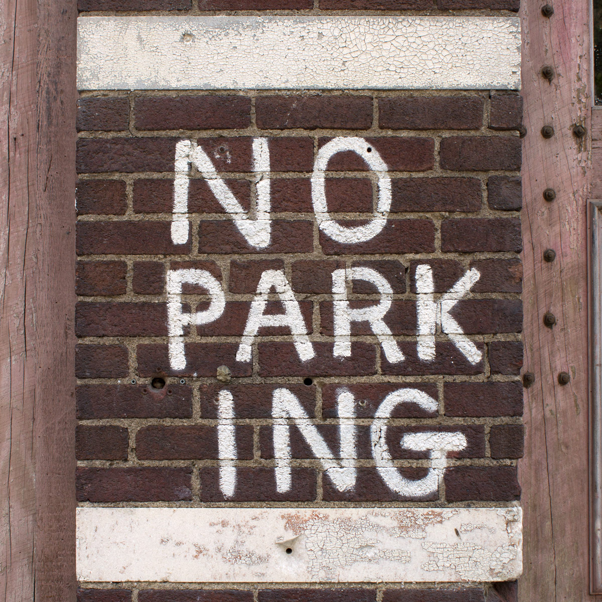 No parking sign where ‘park’ and ‘ing’ have been split up into two words and placed on separate lines so that they could be rendered larger to take advantage of the vertically-narrow space