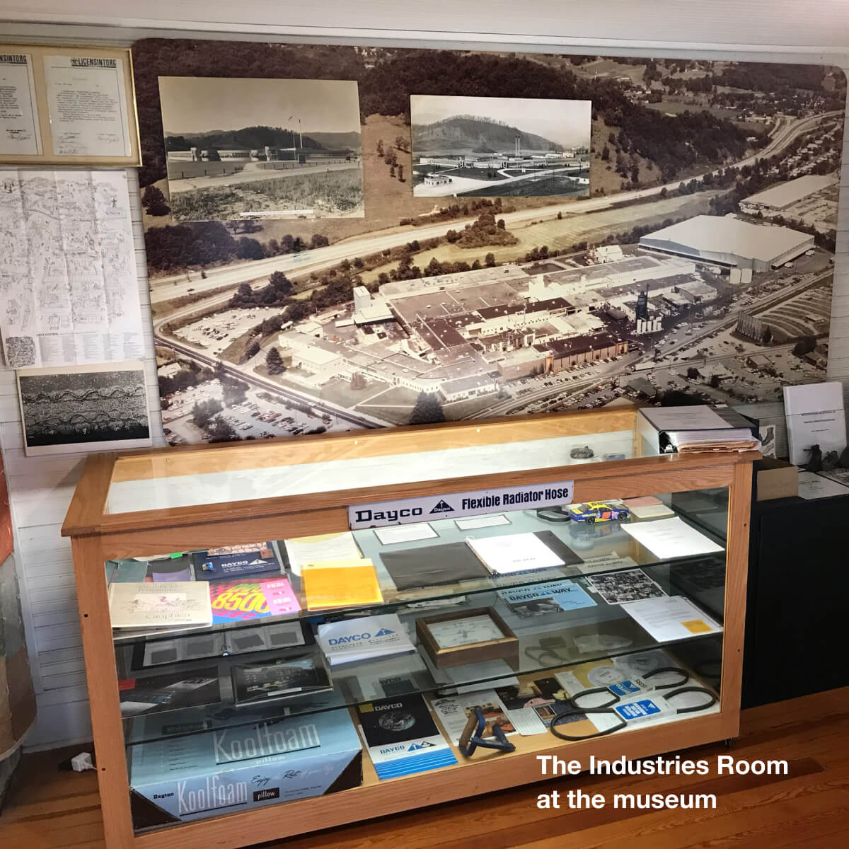 Photo of the ‘Industries Room’ at the Museum of Haywood County History, which contains a large wooden case with artifacts from Dayco Rubber’s Waynesville plant and a large photograph on the wall of the same plant