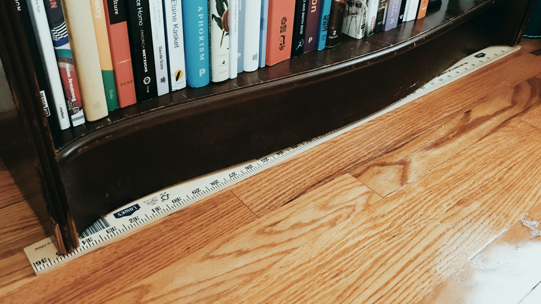 Photograph of a yardstick wedged under a bookshelf to keep it level